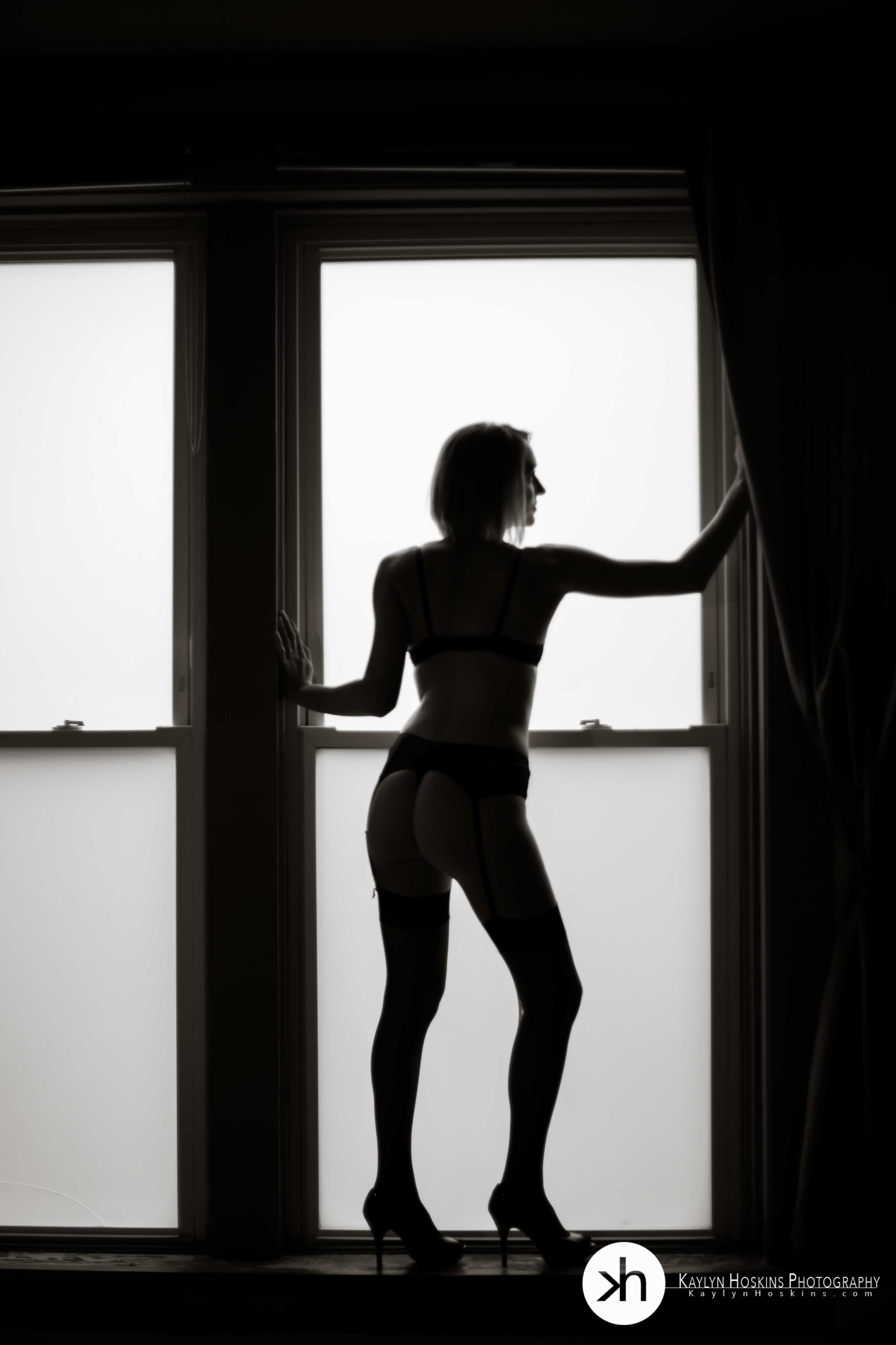 beautiful woman standing in large window during boudoir session
