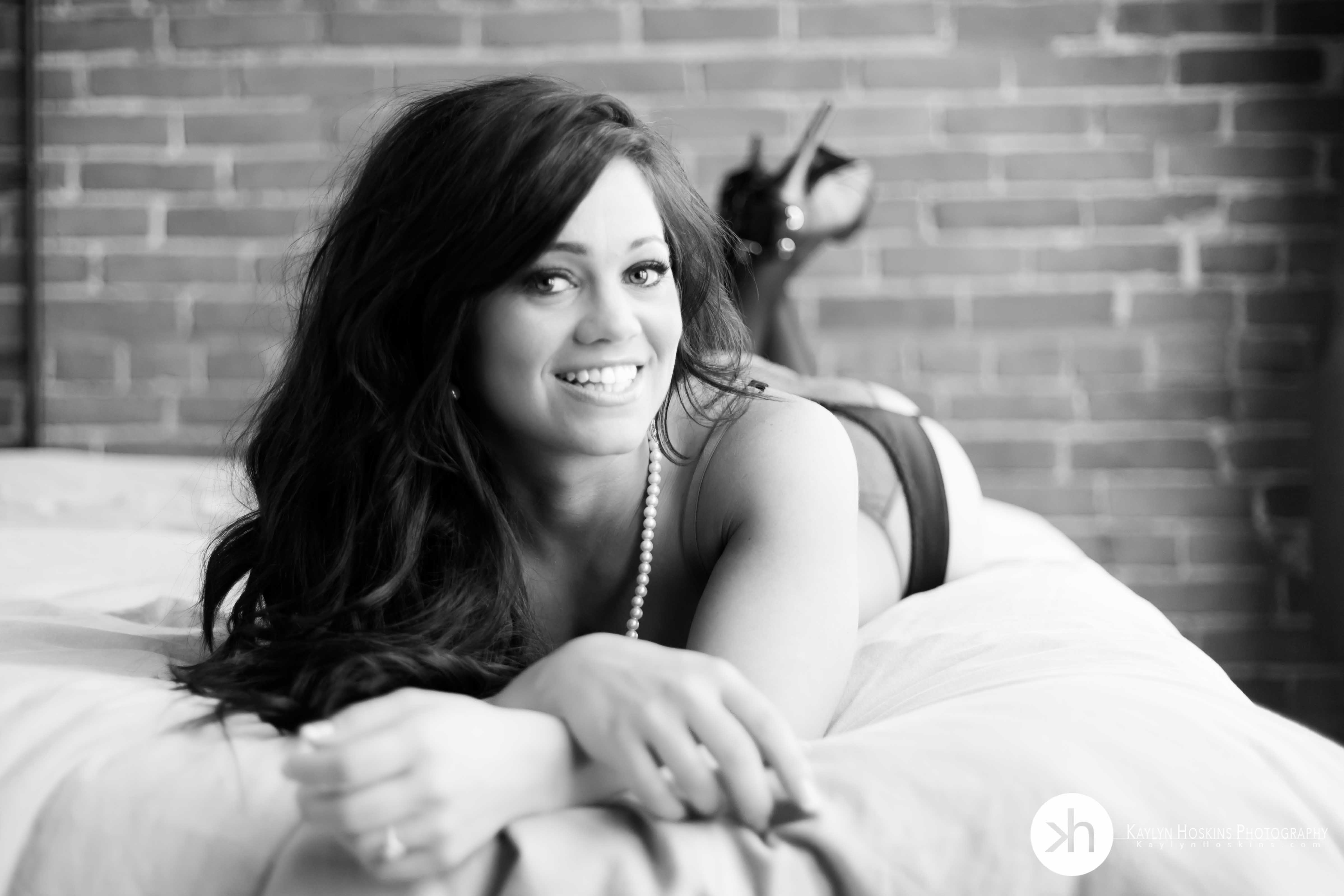 bride to be Arissa in lingerie & stilettos laying on bed during bridal boudoir experience