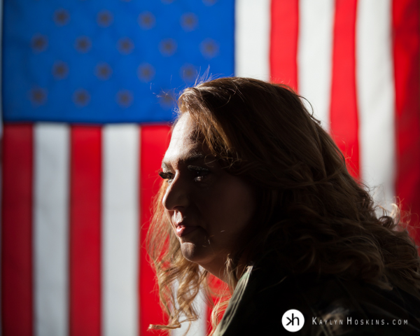 Bad Ass Boudoir Vet Goddess Genevieve looking to the left with american flag behind her