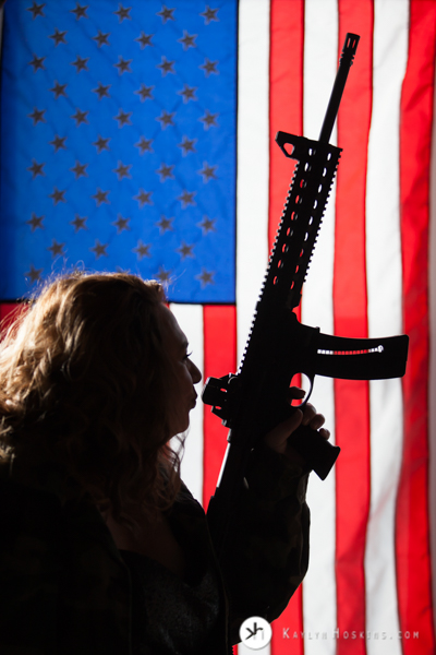 Female Military vet silhouetted holding gun with american flag background  