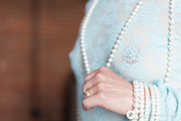 Boudoir Goddess holding on to pearl necklace wearing see thru lacy blue top during boudoir experience in Solon, Iowa