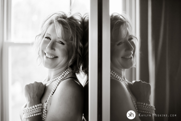 Boudoir Goddess reflecting smiles at camera holding pear necklace during boudoir shoot at Kaylyn Hoskins Photography