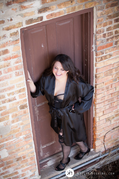 Boudoir Goddess stands outside in rad doorway wearing lingerie and silky black robe 