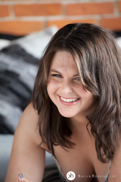 Boudoir Goddess grins big while laying on bed during boudoir shoot at Kaylyn Hoskins Photography