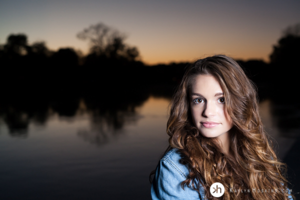 Junior Rower Aurora stands on the dock with sunset behind her during senior photo session at P. Sue Beckwith, M.D. Boathouse in Iowa City