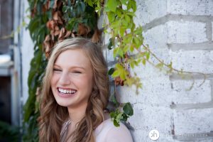 Gorgeous high school senior leaning up against brick wall laughing during senior photo session in Iowa City