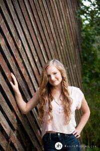 Gorgeous Senior leans up against old barn during senior photo shoot