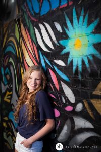 High School Senior smiling, while leaning on rad graffiti wall downtown iowa city behind studio 13