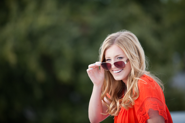 Homecoming Queen wears orange shirt while tipping her sunglasses down while looking at camera