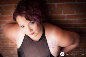 Gorgeous Curvy Girl leaning against brick wall in body suit looking up at camera during boudoir shoot