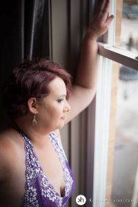 Gorgeous Curvy girl in purple lingerie looking out big front window during boudoir shoot