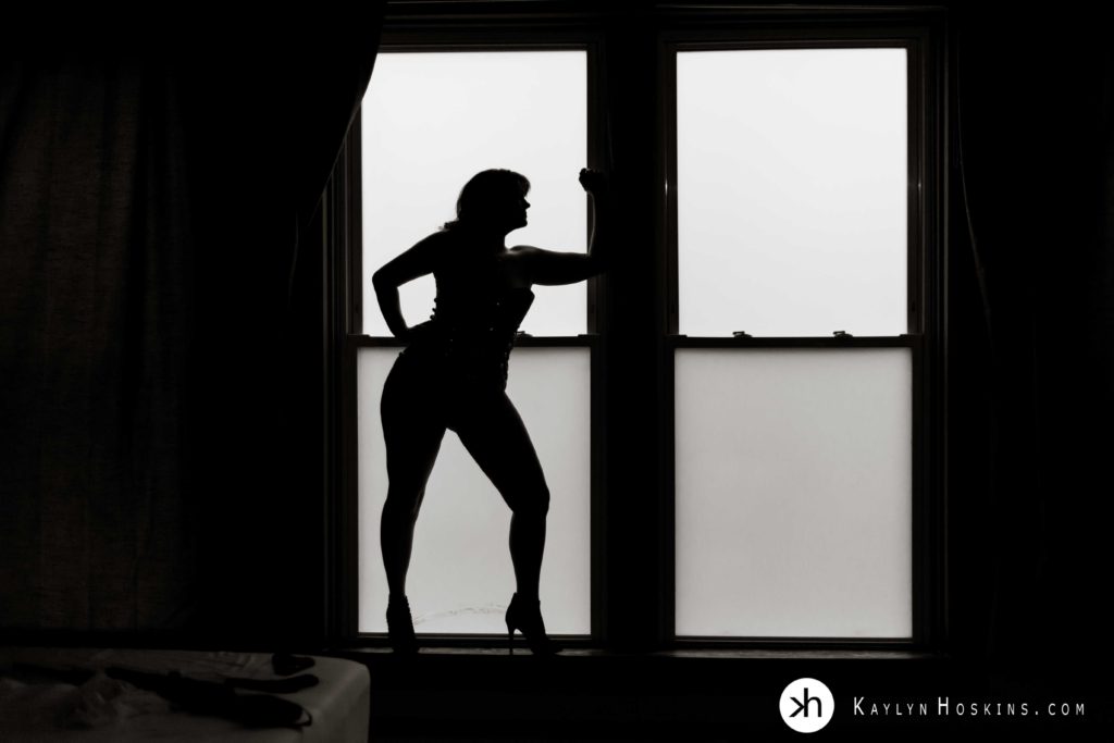 Silhouette of curvy woman in large window during boudoir experience