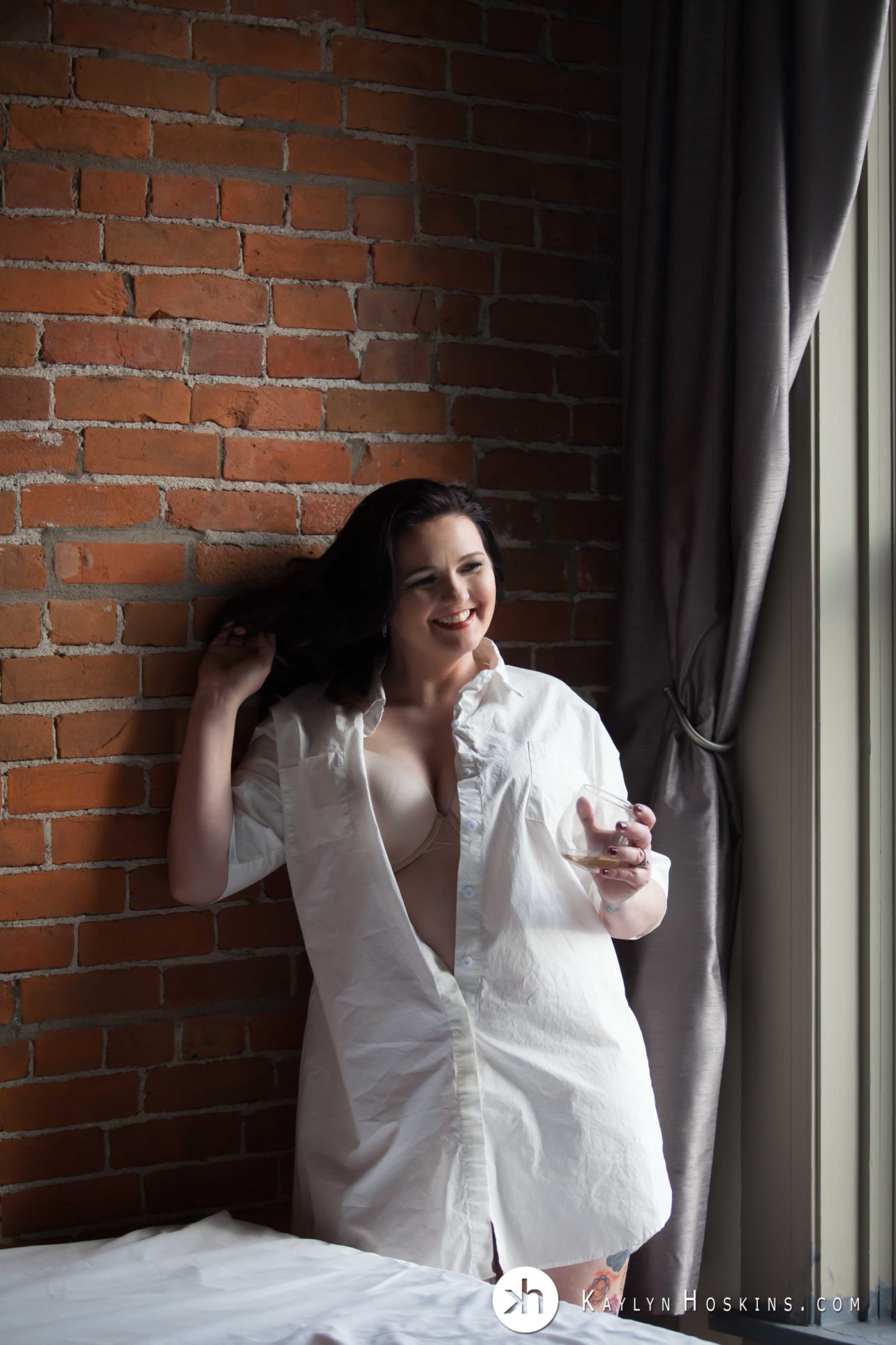 Curvy beautiful woman wearing man's button down shirt while leaning up on brick wall laughing