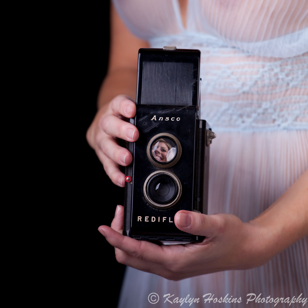 Boudoir client in vintage lingerie looks down thru vintage Ansco rediflex camera