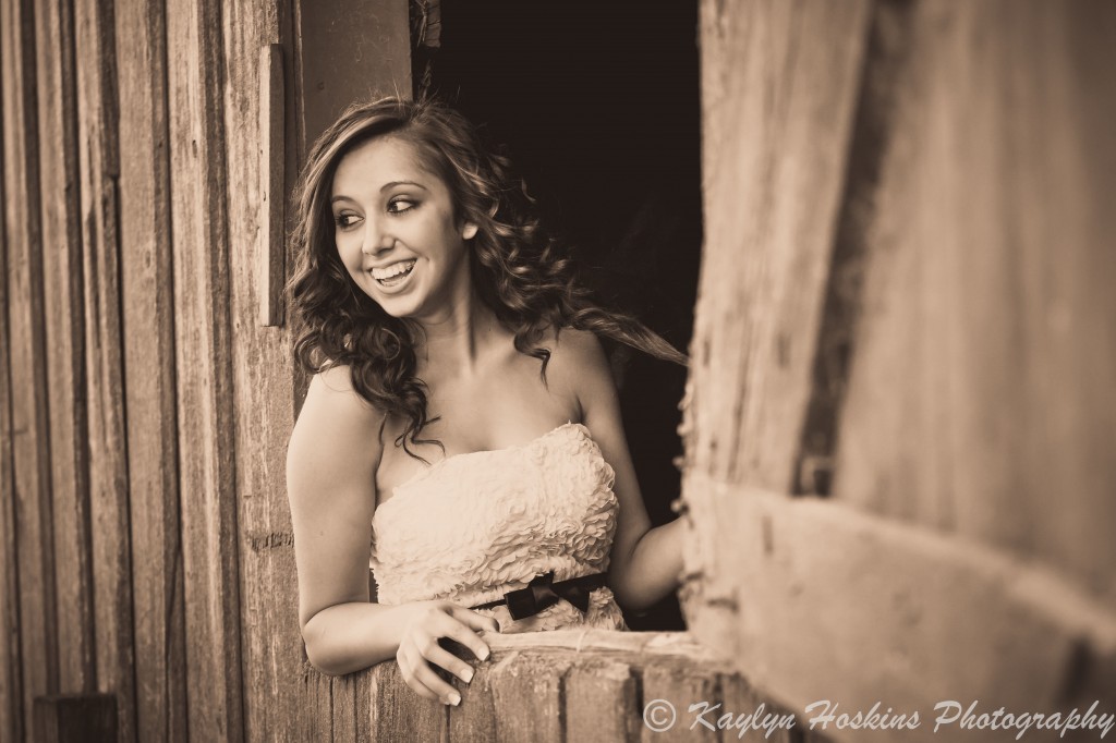 Beautiful Senior laughing while looking out old barn window during senior pics