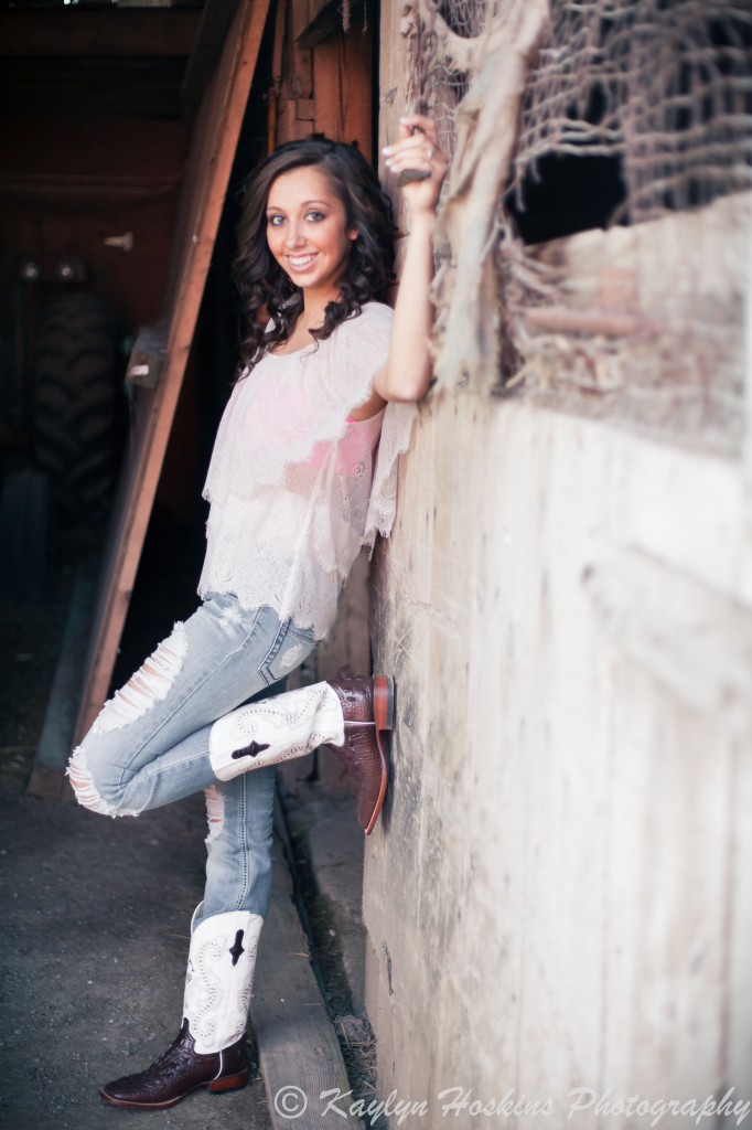 Beautiful Senior leans up against wall in old barn she grew up playing in during her Senior Pictures with Kaylyn Hoskins Photography