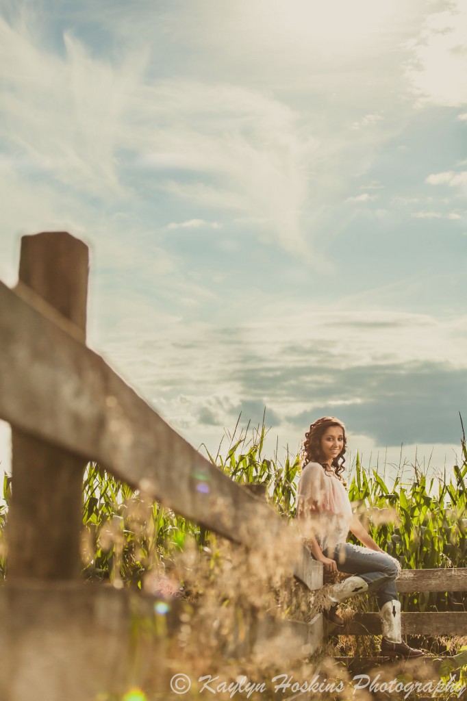 Solon senior sits on fence in front of corn field during her senior pics with Kaylyn Hoskins Photography