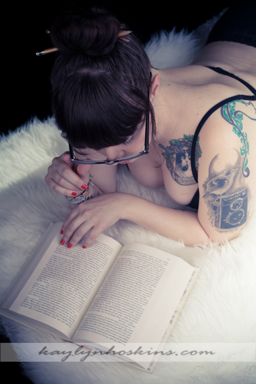 Ms. F reads her book laying on a white fur rug during her boudoir session with Kaylyn Hoskins Photography