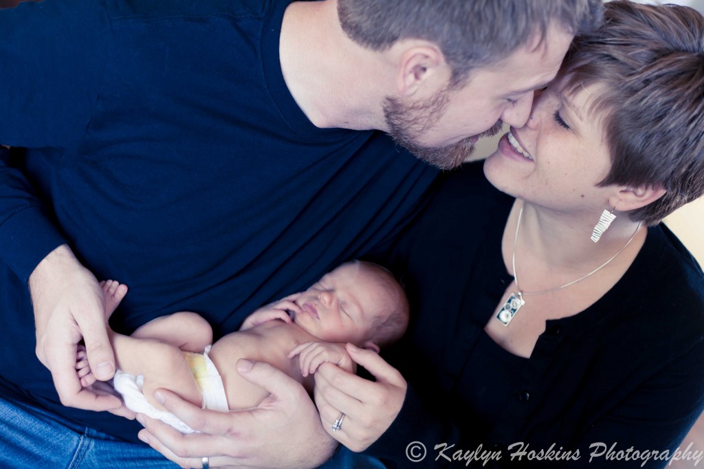 new Mom and Dad kissing as they hold their brand new baby boy