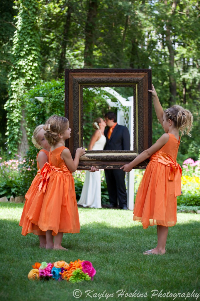 Beautiful bridesmaids hold a beautiful frame in front of the bride and groom outside the Little Brown Church