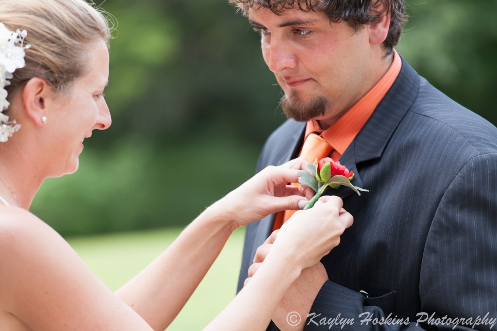 Bride pins on groom's corsage before wedding ceremony at The Little Brown Church in Nashua