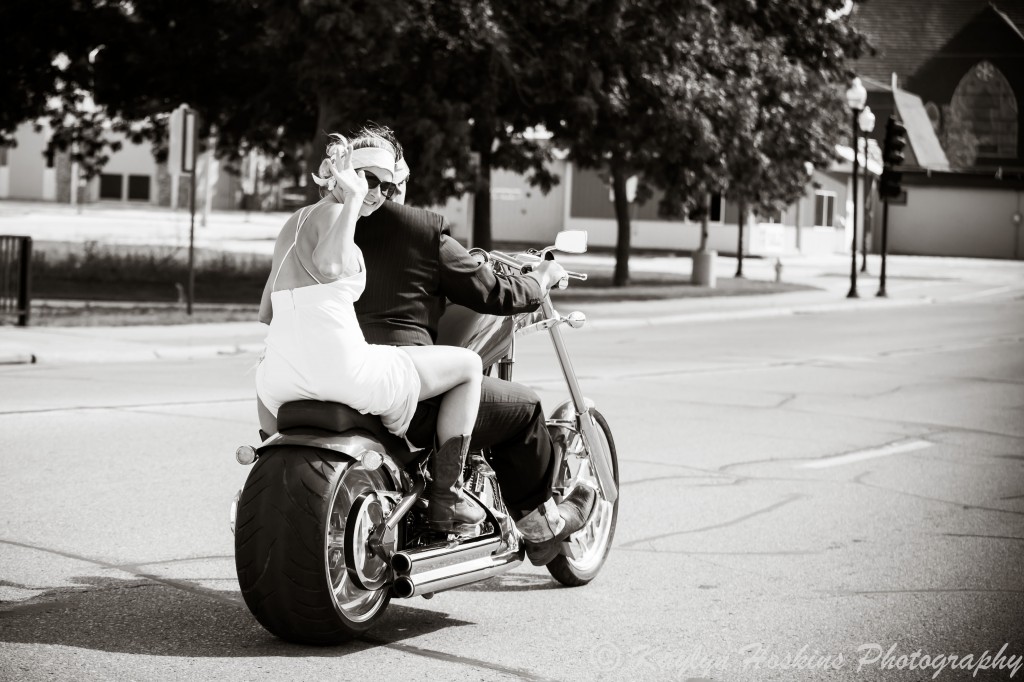 Bride waves as the groom zooms away on a Harley to get to their wedding reception in Iowa