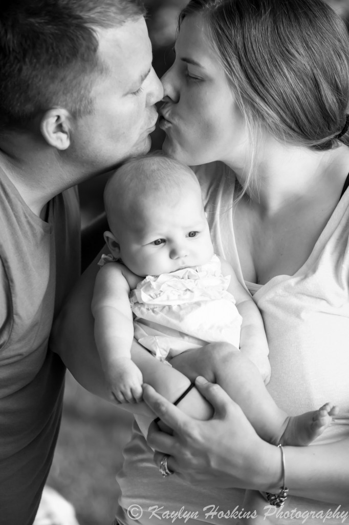 Mom and Dad kiss above baby during family photos